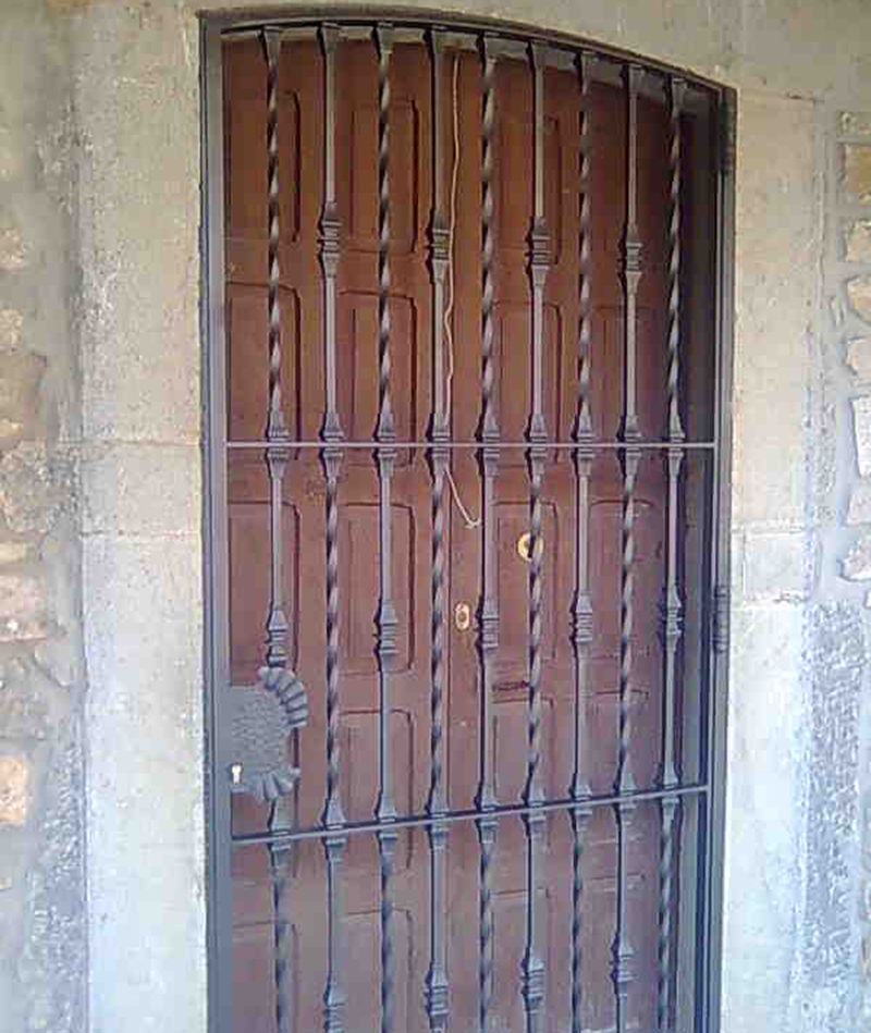 Puerta de forja con barrotes en la entrada de una casa.